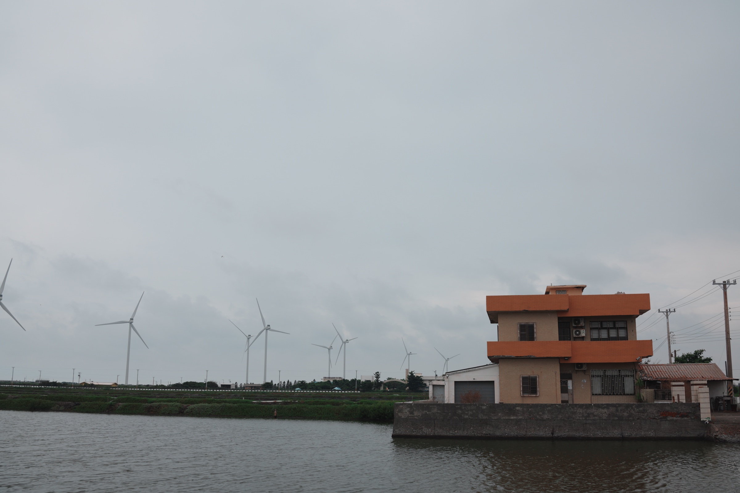 A coastal house, fish ponds, and a row of utility-scale land wind turbines in Fangyuan